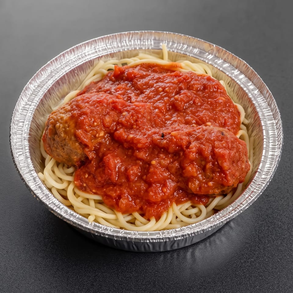 Spaghetti topped with meatballs and chunky tomato sauce served in a disposable aluminum bowl.