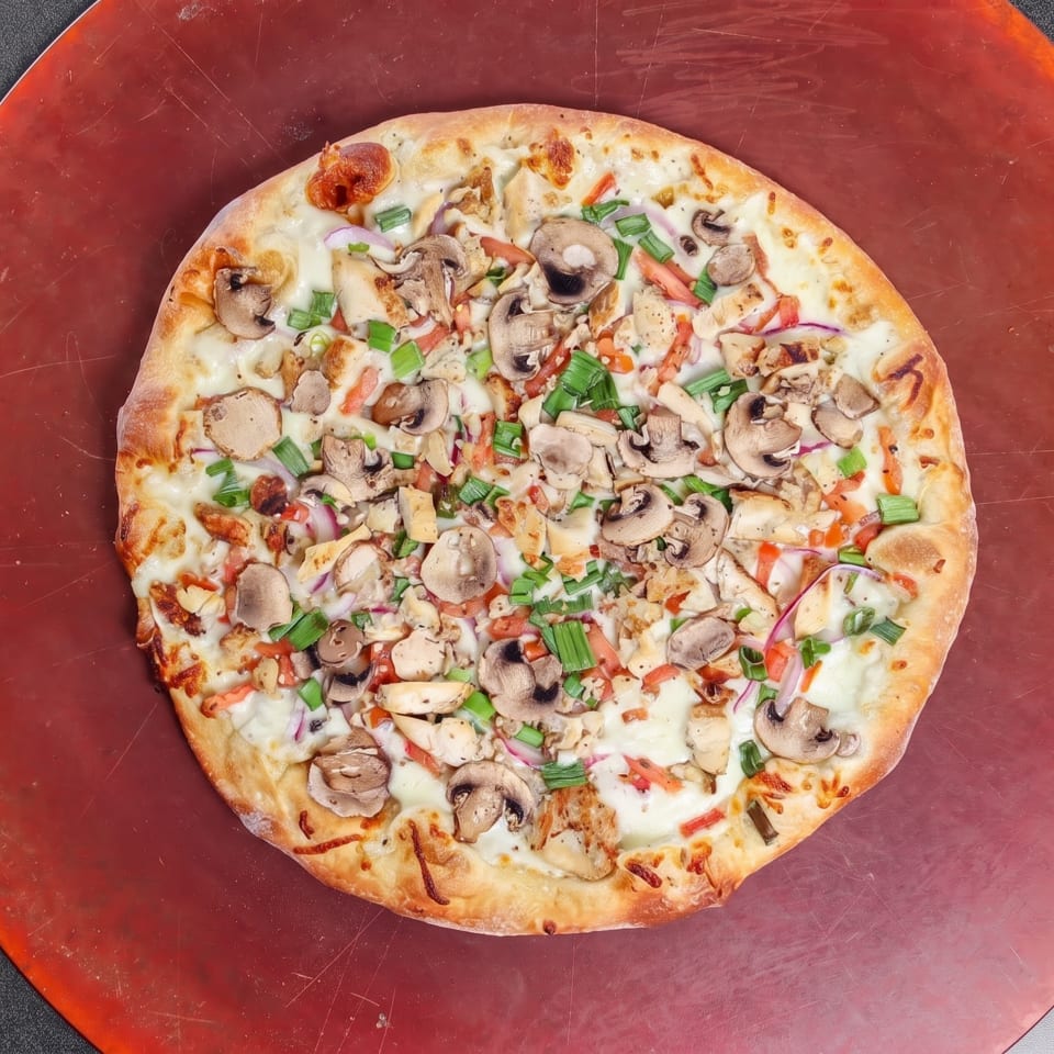 Vegetable and chicken pizza topped with mushrooms, green onions, peppers, red onions, and melted cheese on a red pizza board.